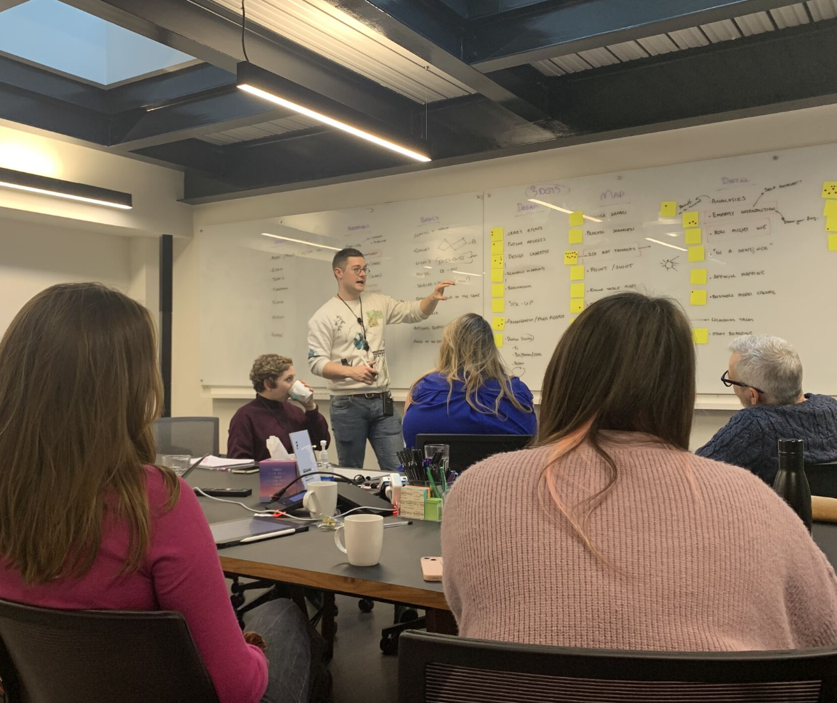 A group of people in a workshop room around a table covered in sticky notes.